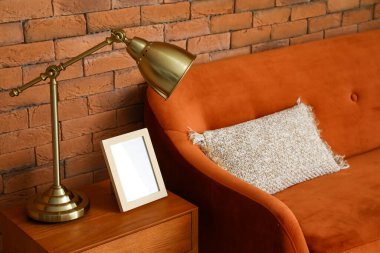 Altın lamba, ahşap masa ve tuğla duvarın yanındaki kanepe.