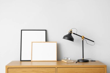 Işık duvarının yanındaki masada siyah lamba, gözlük ve çerçeveler.