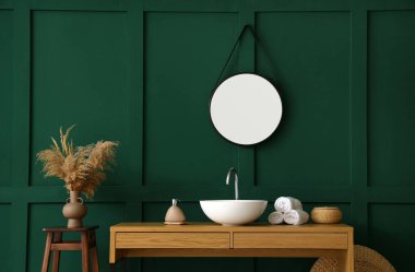 Banyoda yeşil duvarın yanında lavabo, sabun ve havlu olan masa.