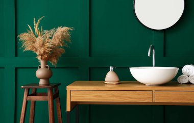 Ahşap masa, lavabo, sabun ve temiz havlular yeşil duvarın yanında.