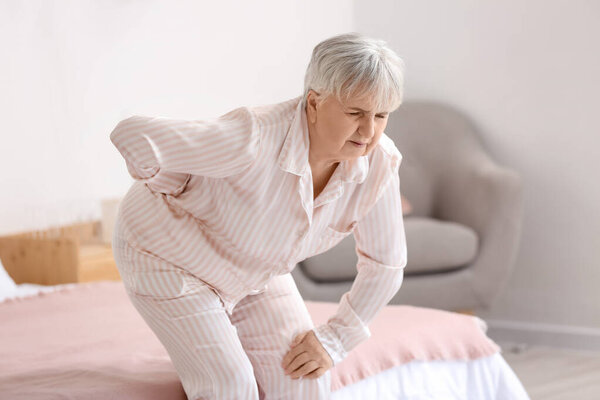Senior woman suffering from back pain near bed at home