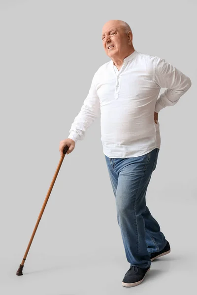 軽い背景で背中の痛みに苦しんで歩く棒を持つシニア男 — ストック写真