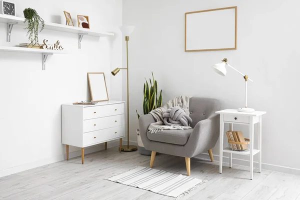 Interior of light living room with lamps, armchair and commode