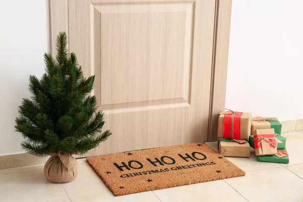 Мат Рождественским Поздравлением Подарками Елкой Возле Светлой Деревянной Двери — стоковое фото