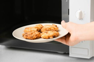 Kadın, mutfaktaki mikrodalga fırına yumuşatılmış bifteklerle tabak koyuyor.