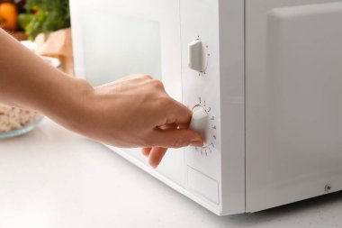 Kadın mutfakta beyaz mikrodalga fırını ayarlıyor.