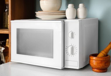 Mavi duvarın yanında mutfak gereçleri olan beyaz mikrodalga fırın.