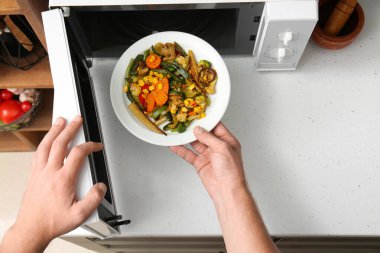 Mutfakta mikrodalga fırından sebzeli tabak alan bir kadın.