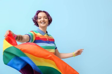 Mavi arka planda LGBT bayrağı olan genç bir kadın.