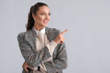 Gri arka planda bir şeye işaret eden zarif bir kadın.