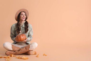 Güzel, gülümseyen bir kadın balkabağı tutuyor ve renkli arka planda oturuyor.