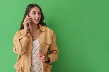 Yeşil arka planda cep telefonuyla konuşan genç bir kadın.