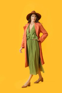 Sarı arka planda şık sonbahar kıyafetleri içinde güzel, gülen bir kadın.