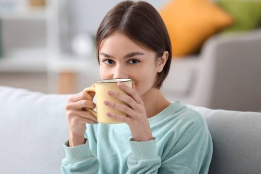 Güzel genç bayan evdeki kanepede çay içiyor.