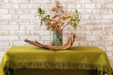 Sonbahar dalları ve açık tuğla duvarın yanındaki masada geyik boynuzu olan vazo.