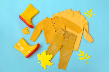 Şık çocuk kıyafetleri, çizmeleri ve mavi arka planda sonbahar yaprakları.