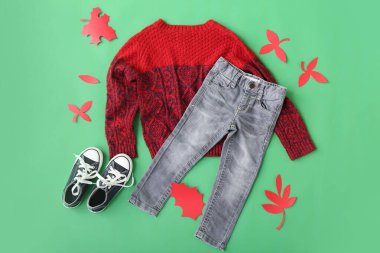 Şık çocuk süveteri, kot pantolon, ayakkabı ve arka planda sonbahar dekoru