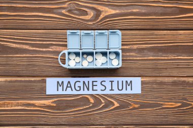 Farklı haplara ve tahta arka planda MAGNESIUM kelimesine sahip plastik konteynır