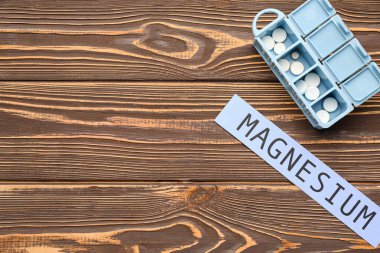 Farklı haplara ve tahta arka planda MAGNESIUM kelimesine sahip plastik konteynır