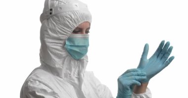 Koruyucu kıyafetli doktor beyaz arka plana lastik eldiven takıyor.
