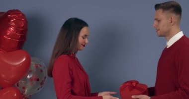 Sevgililer Günü 'nde gri arka planda sevgilisini selamlayan hediyeli genç bir adam.