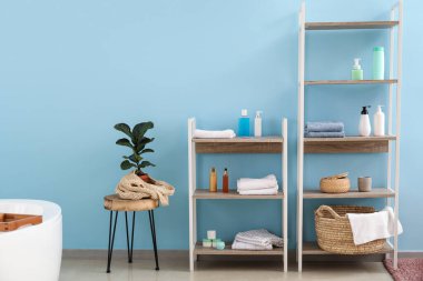 Mavi duvarın yanında banyo malzemesi olan raflar.