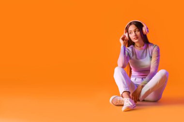 Renkli arka planda müzik dinleyen havalı genç bir kadın.