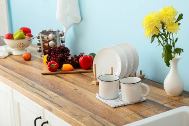 Çiçekli vazo, fincanlar ve tabaklar mavi duvarın yanındaki ahşap masada.