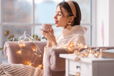 Güzel genç bayan evdeki kanepede çay içiyor.