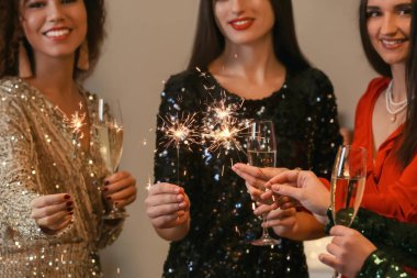 Evde Noel 'i kutlamak için maytap ve bir bardak şampanya taşıyan güzel genç kadınlar.