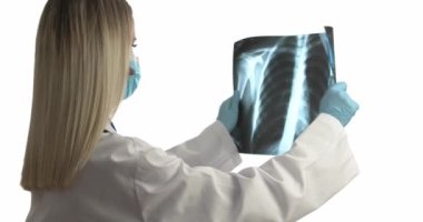 Tıbbi maskeli doktor beyaz arka planda akciğerlerin röntgen görüntülerini inceliyor.
