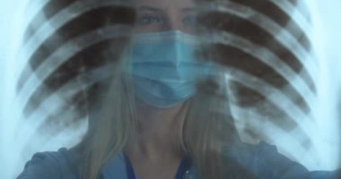 Tıbbi maskeli doktor akciğerlerin röntgen görüntülerini inceliyor.