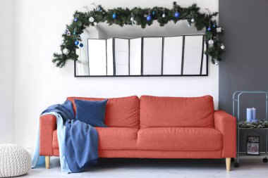 Modern oturma odasının içinde mercan kanepesi ve Noel dallarıyla süslenmiş büyük bir ayna.