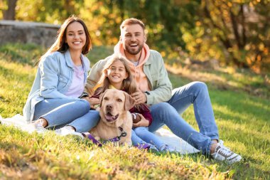 Labrador köpeğiyle mutlu bir aile parkta ekose üzerinde oturuyor.