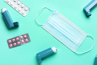 Tıbbi maske, astım spreyi ve renkli arka planda haplar, yakın plan.