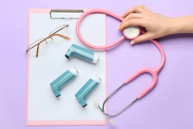 Kadın eli, pano, gözlük, steteskop ve astım spreyleri.