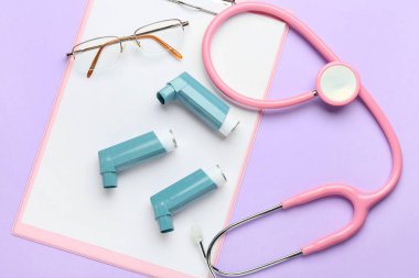 Renk arkaplanında pano, gözlük, steteskop ve astım spreyleri, yakın plan