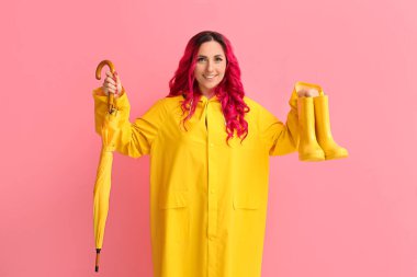 Renkli çizmeleri ve şemsiyesi olan yağmurluk giymiş güzel bir kadın.