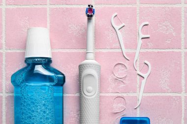 Kürdanlı diş ipi, elektrikli fırça ve pembe fayanslı durulama.