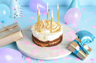 Lezzetli doğum günü pastası, balonlar ve mavi arka planda hediyeler.