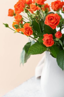 Masanın üzerinde turuncu güller olan vazo bej duvara yaslanmış, yakın plan.
