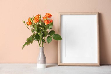 Güzel turuncu güller ve bej duvarlı boş fotoğraf çerçeveli vazo.