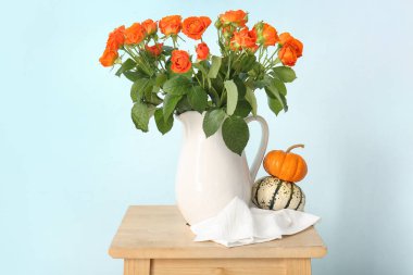 Mavi duvarda güzel turuncu güller ve balkabakları olan sürahi.