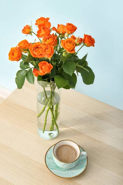 Wazon Pięknymi Pomarańczowymi Różami Filiżanką Kawy Stole Przed Niebieską Ścianą — Zdjęcie stockowe