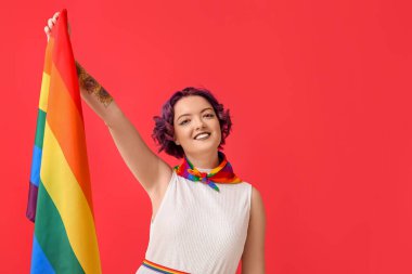 Kırmızı arka planda LGBT bayrağı olan genç bir kadın.