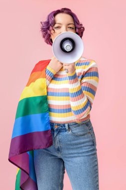 Pembe arka planda LGBT bayrağı ve megafonu olan genç bir kadın.