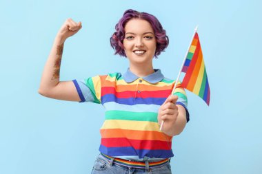Mavi arka planda LGBT bayrağı olan genç bir kadın.