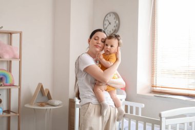 Genç anne küçük bebeğini yatak odasında tutuyor.