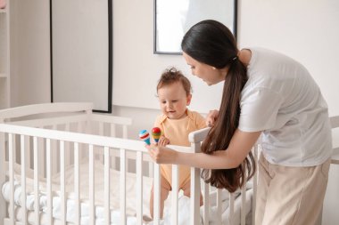 Genç anne beşikteki bebeğine oyuncak veriyor.
