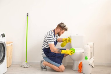 Tuvaleti süngerle temizleyen genç bir adam.